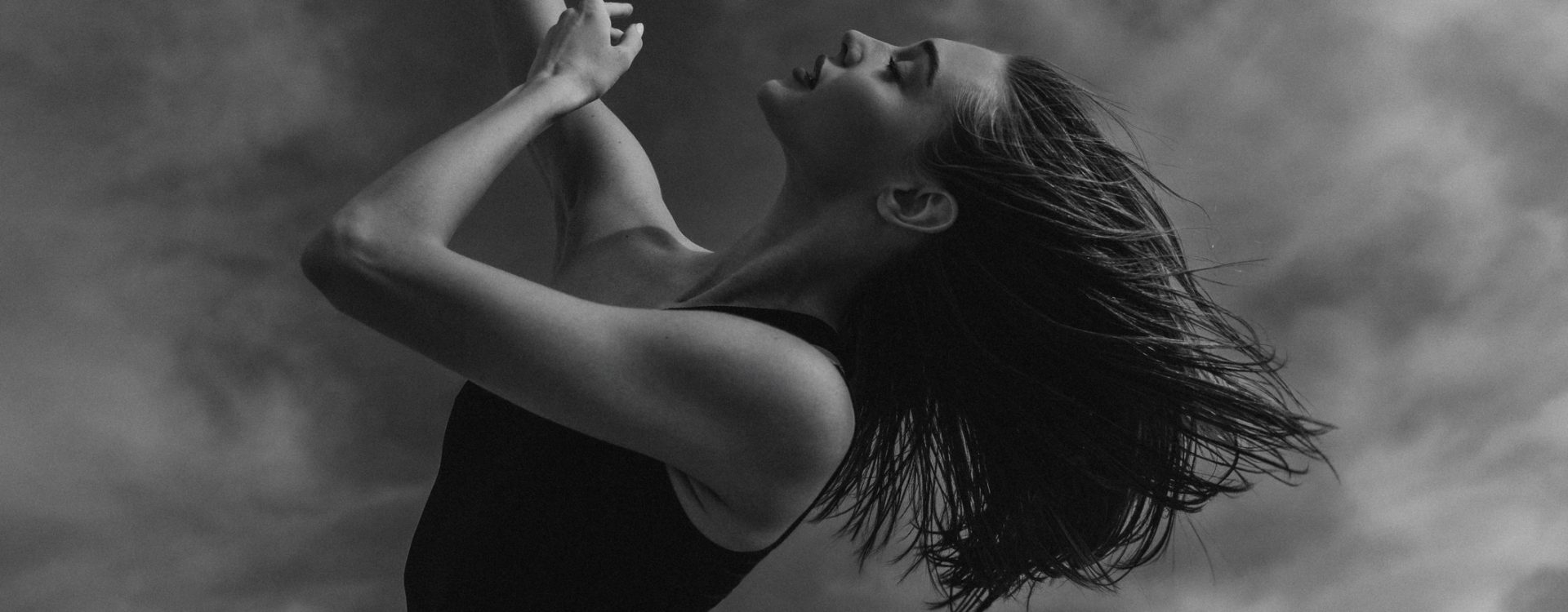 Woman in movement captured in artistic black-and-white portrait against dramatic sky