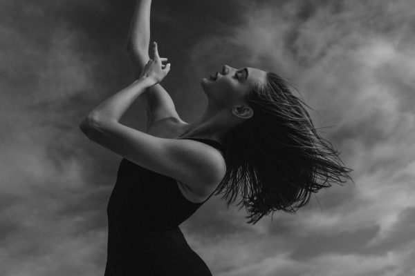 Woman in movement captured in artistic black-and-white portrait against dramatic sky
