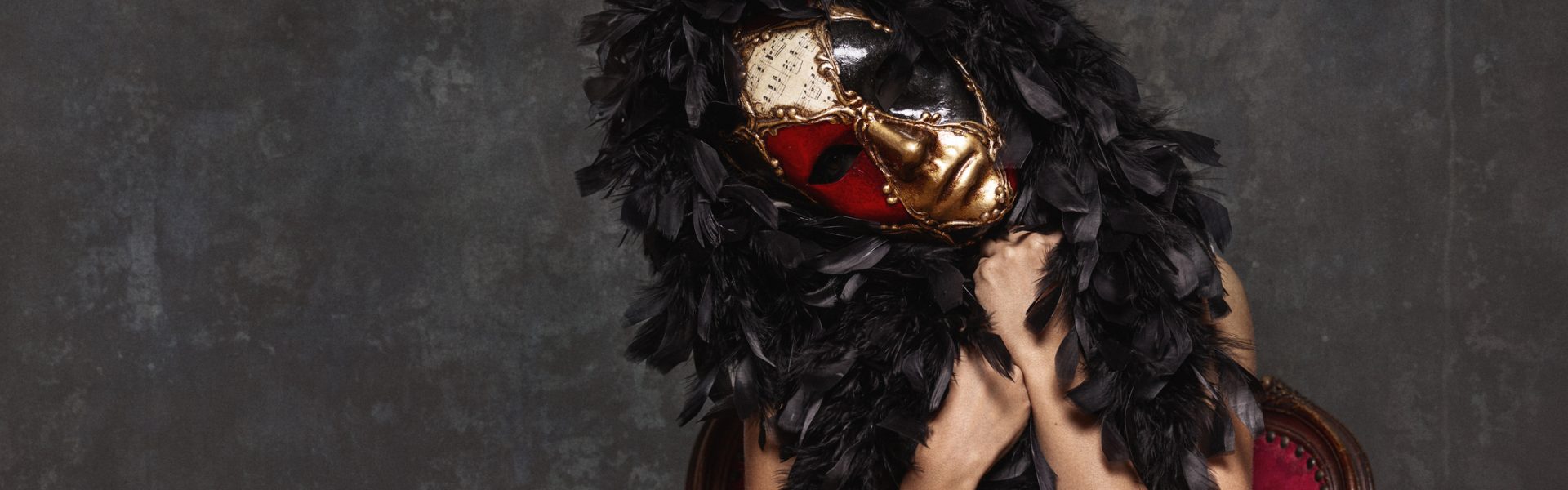 Elegant Masked Figure Draped In Feathers Sitting On A Vintage Chair